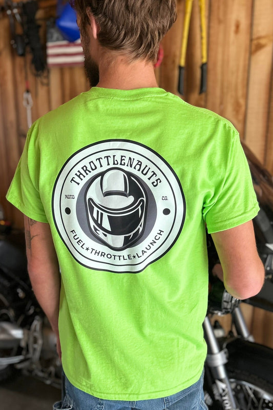 Person wearing a lime green t-shirt with a motorcycle helmet graphic and text in a garage setting.