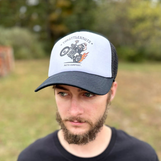 Man wearing a cap and black shirt with a brand logo, standing outdoors.